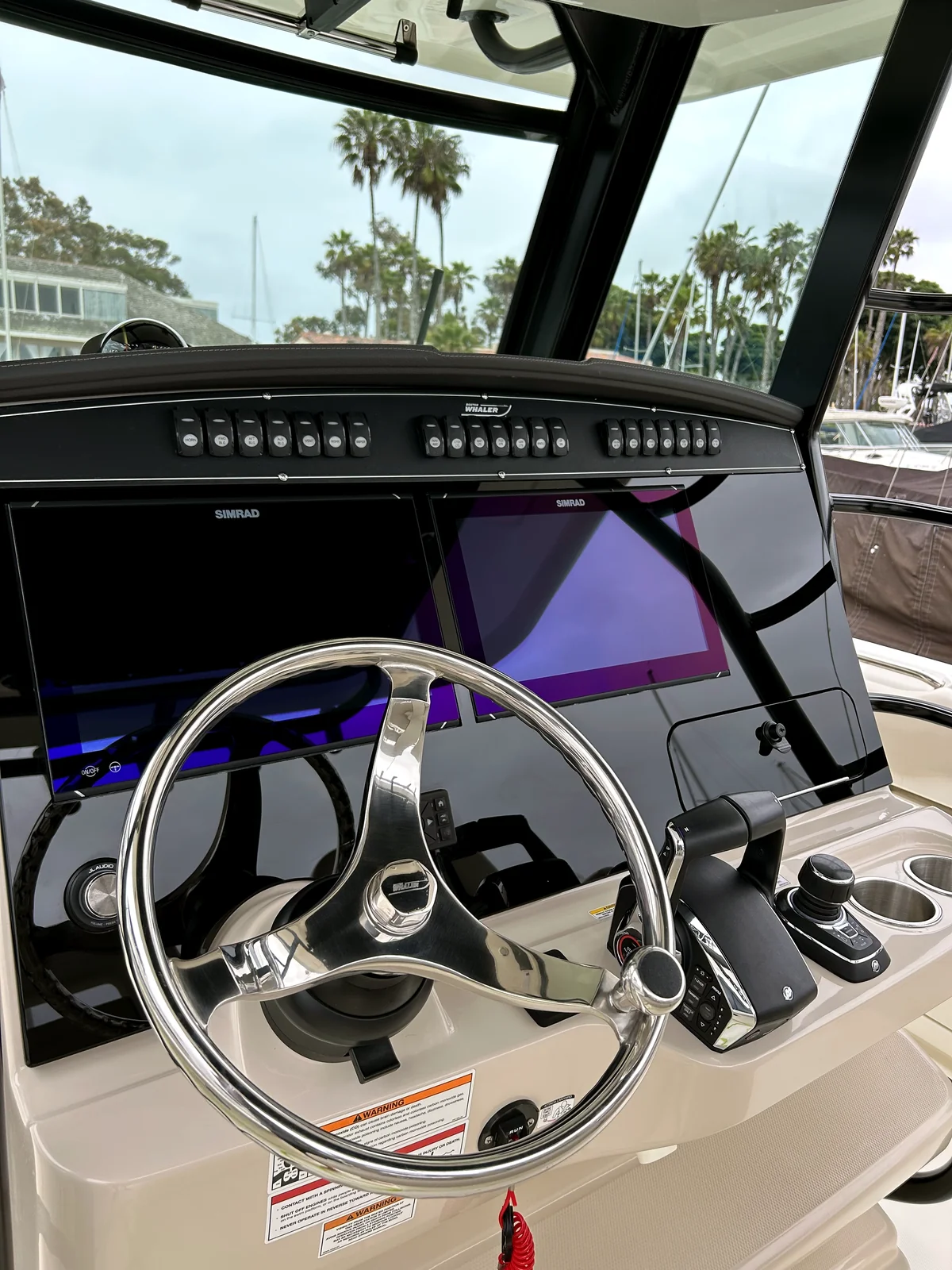 Yacht helm and electronics with San Diego palm trees visible through the windshield